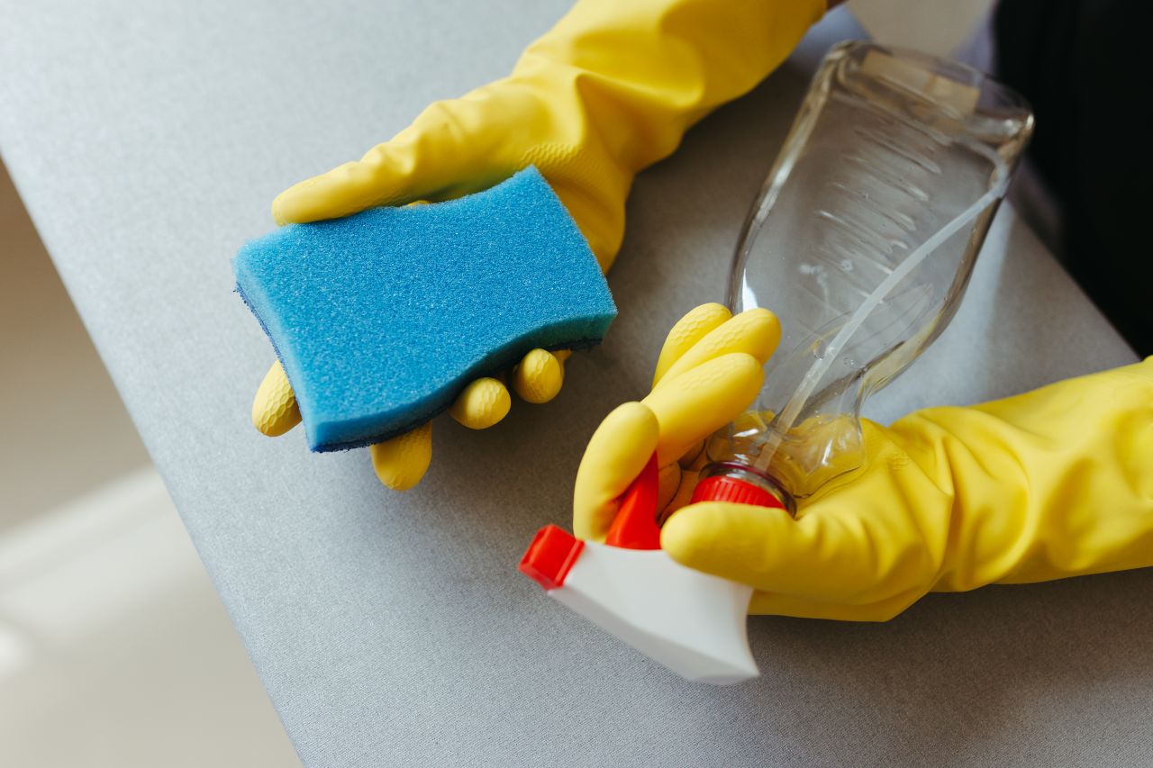 hero-img-02 Close-up of hands in gloves holding a sponge and spray bottle for cleaning.